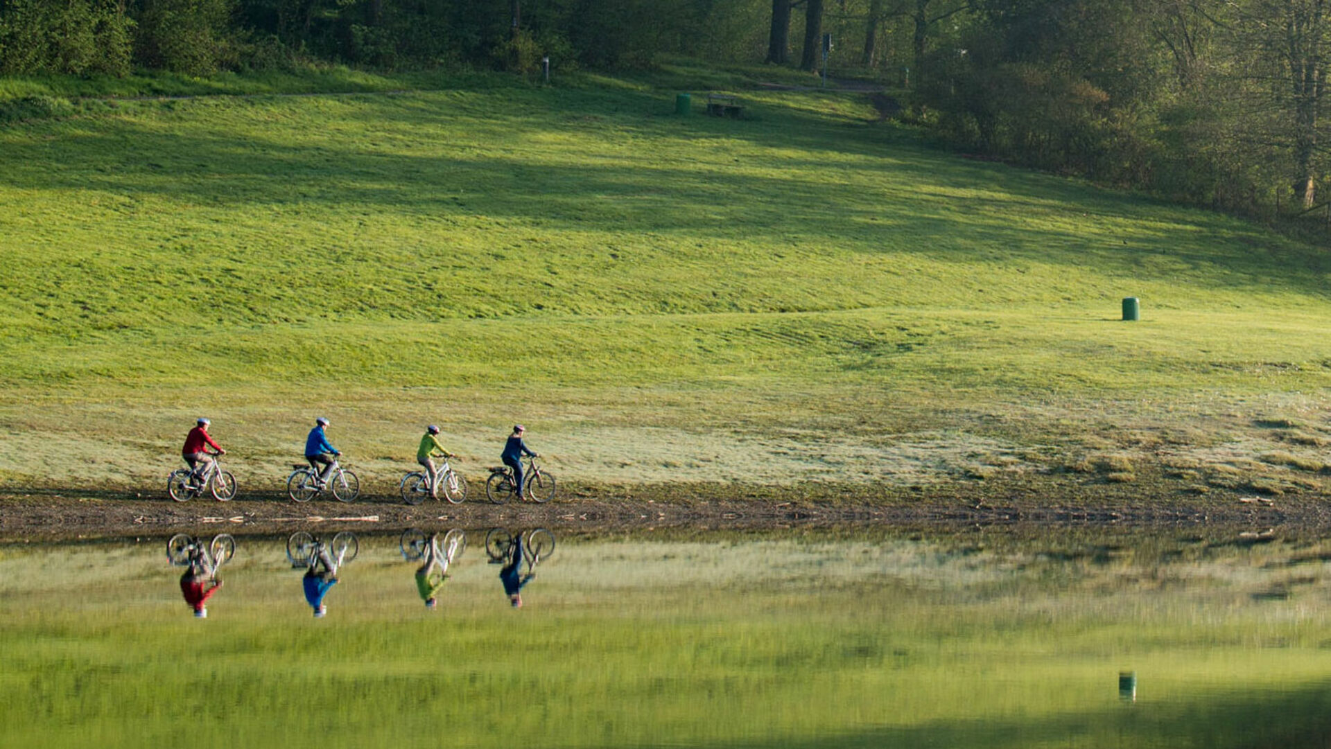 Radfahrer und Bäume spiegeln sich im Hennesee bei Meschede im Sauerland